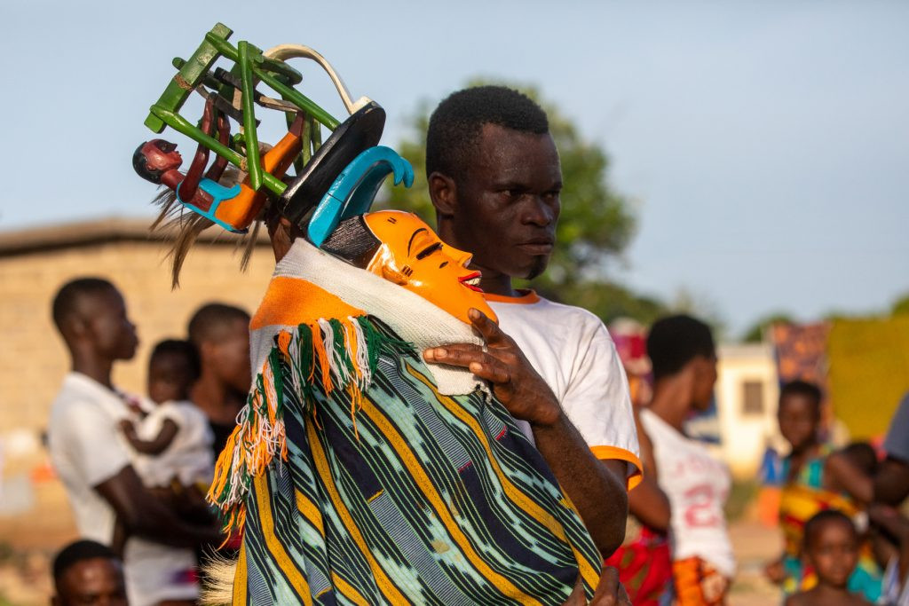 Zaouli Dancer and Guardian Preparing for Performance in Bouaflé, Ivory Coast: A Zaouli dancer, guided by his guardian, awaits the cue to begin his captivating performance for the eager audience.