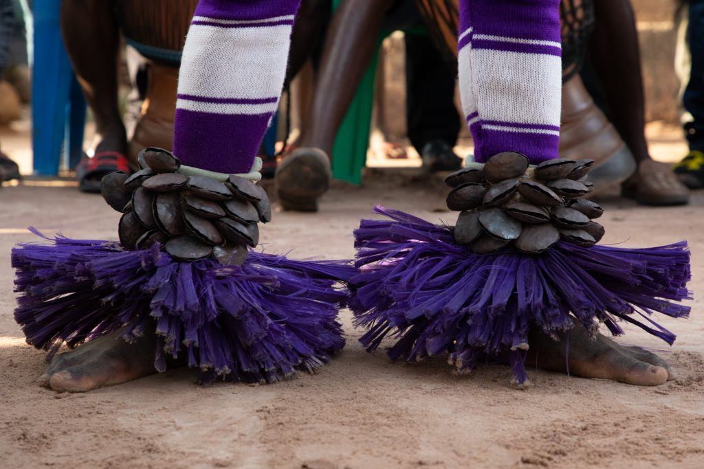 Traditional Zaouli Dance Costume Detail: Raffia anklets and metal bells adorn the legs of a Zaouli dancer, enhancing the rhythmic sounds of this Ivorian dance.
