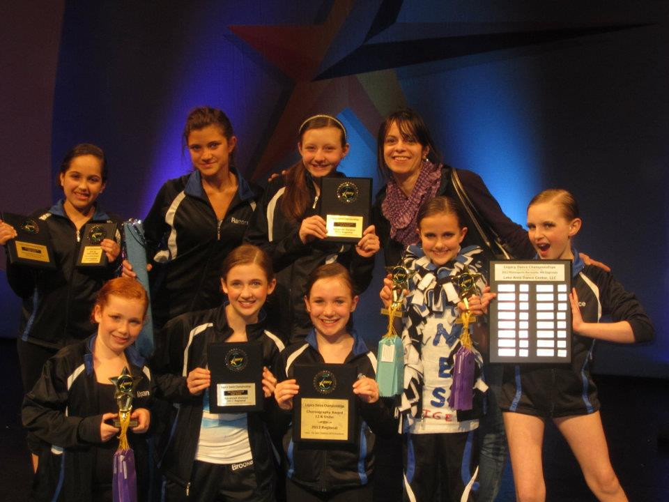 Lake Area Dance Center's dance group proudly displaying their awards at the Legacy Dance Championships, showcasing their studio's success and teamwork.