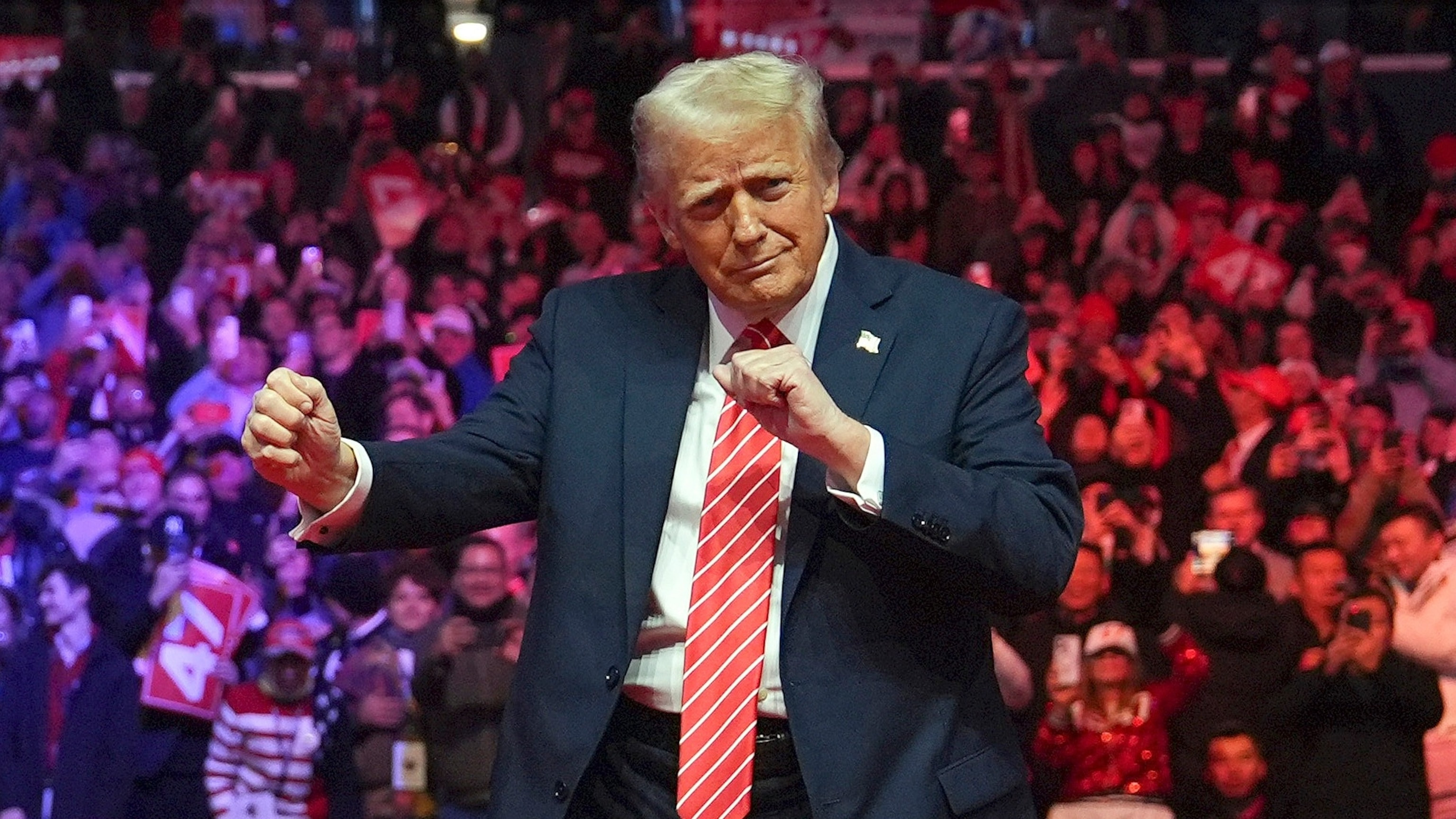 President-elect Donald Trump dancing at a rally, captured from a wide angle showing the stage setup with the Village People and the enthusiastic crowd in the background.