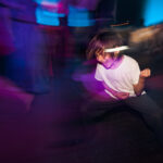 A wedding guest passionately playing air guitar on the dance floor, illuminated by dynamic reception lighting.