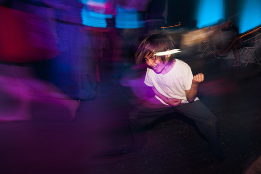 A wedding guest passionately playing air guitar on the dance floor, illuminated by dynamic reception lighting.