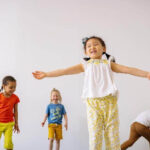 Image features four children laughing and dancing together.