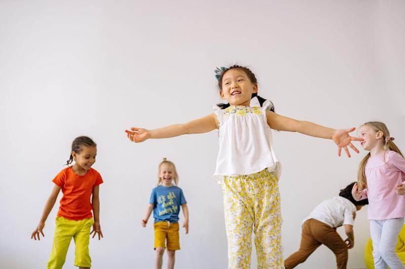 Image features four children laughing and dancing together.