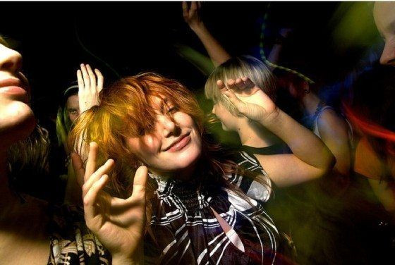 DJ enthusiastically dancing in the booth, surrounded by vibrant lights and a cheering crowd, projecting an image of confidence and infectious energy