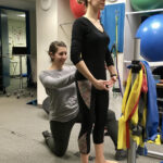 Melissa Buffer adjusts a dancer's back while she stands on circles on the floor, emphasizing the use of strength-training for building lightness.