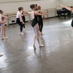 Ballet students practicing a combination, following the instructor's lead, focusing on posture and form