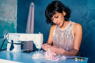 Young woman in a sequins top at a sewing machine, creating dance costumes