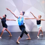 ballerina wearing a black leotard and pink ballet shoes practicing in a dance studio